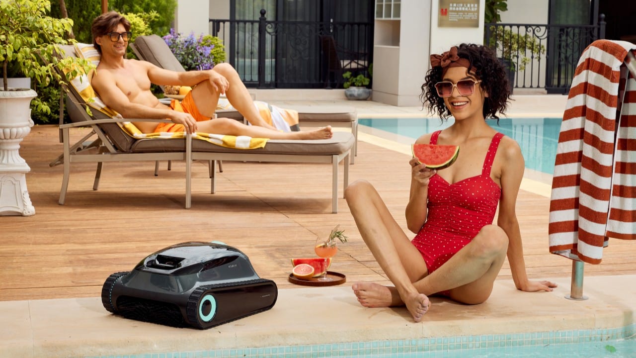 A robotic pool cleaner sits on the edge of a clean, inviting swimming pool with people relaxing nearby, illustrating effortless pool maintenance.